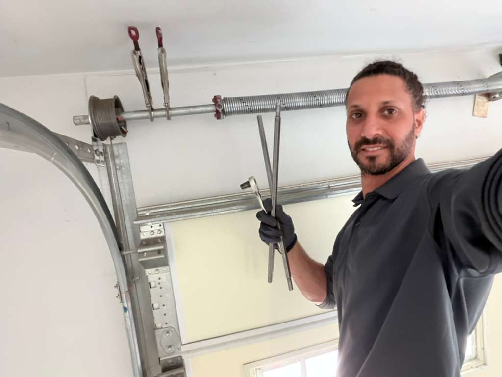 A technician at work on a garage door torsion spring and cable drum