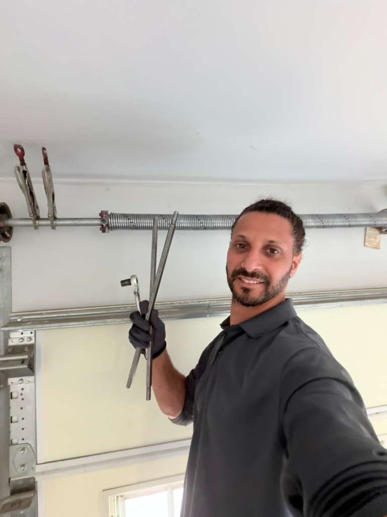 A technician working on a garage door torsion spring with winding bars